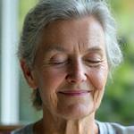 A serene woman practices meditation, eyes closed, with soft natural light illuminating her face. She has an inviting, calm demeanor.